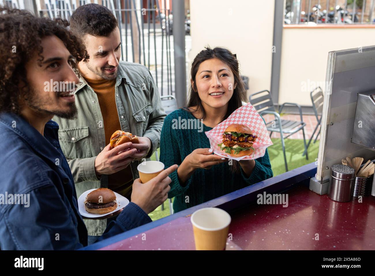 A diverse group of friends shares a moment of joy while eating gourmet street food served from a food truck, showcasing urban lifestyle and friendship Stock Photo