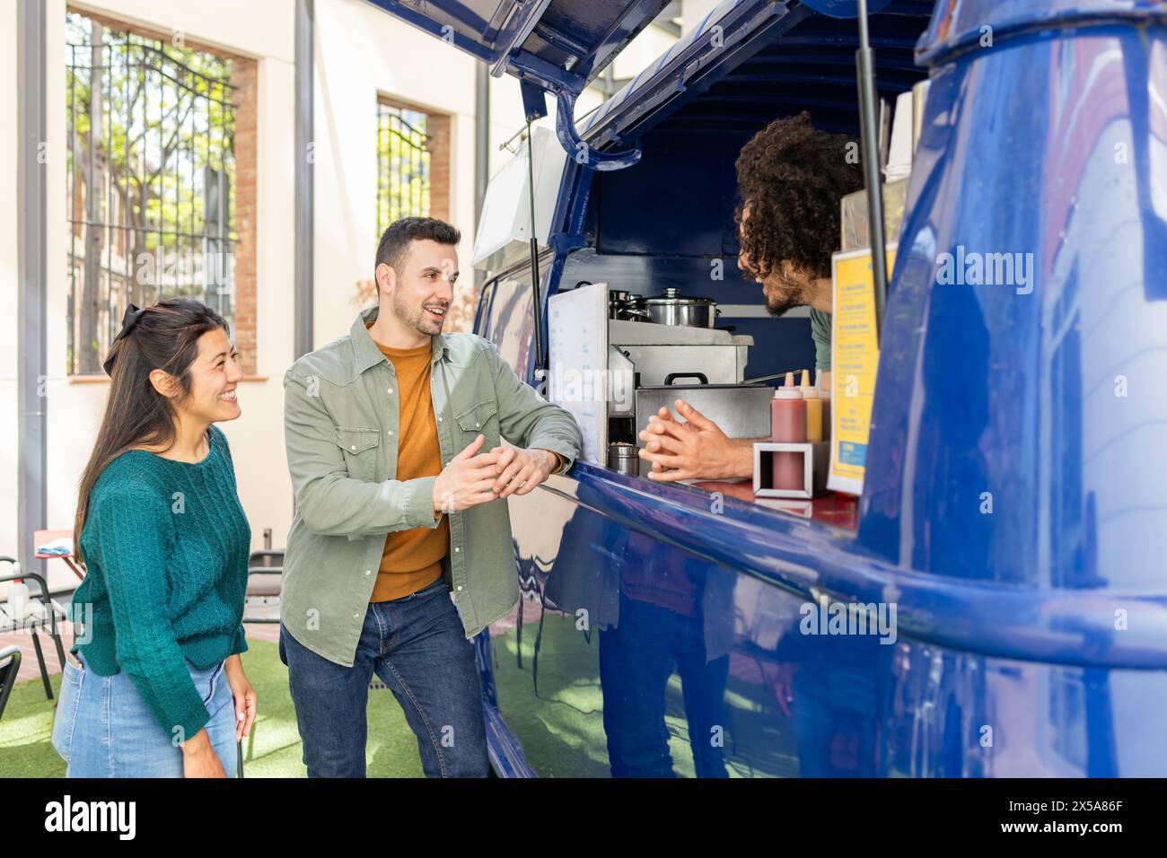Two friends share a cheerful moment while ordering food from a vendor at a vibrant blue food truck Stock Photo