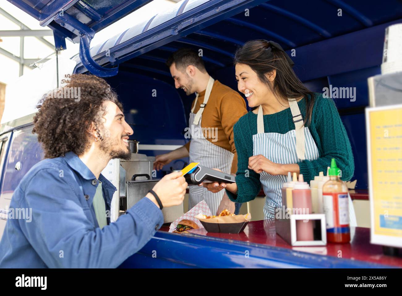 A cheerful customer pays with a card at a vibrant food truck while engaging with friendly staff Stock Photo