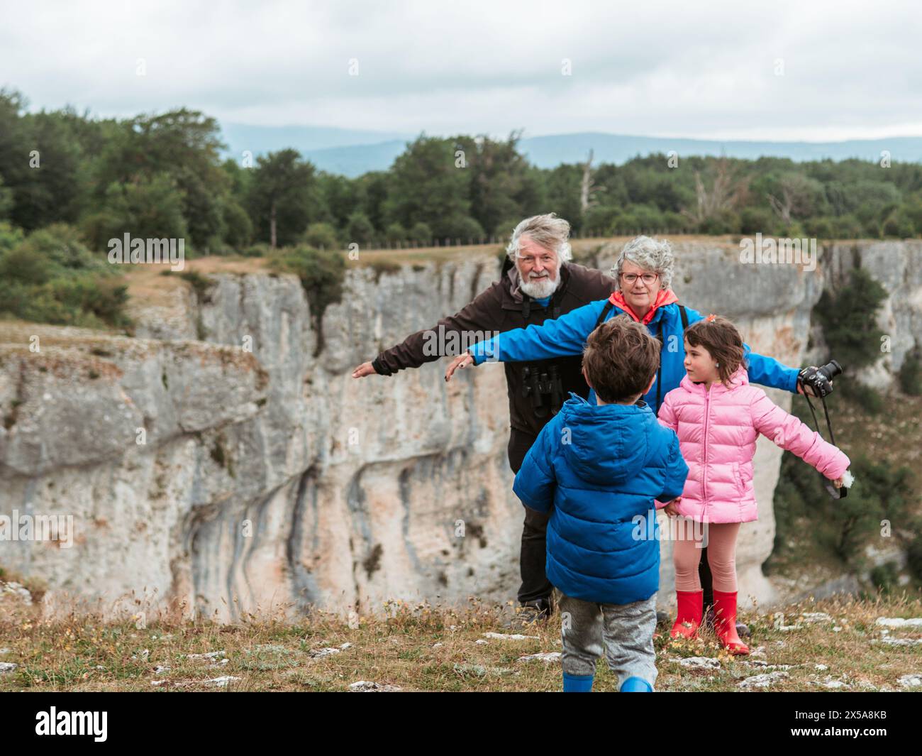 A heartwarming family scene with grandparents and their grandchildren, a boy and a girl, spending quality time together in a natural landscape. Stock Photo