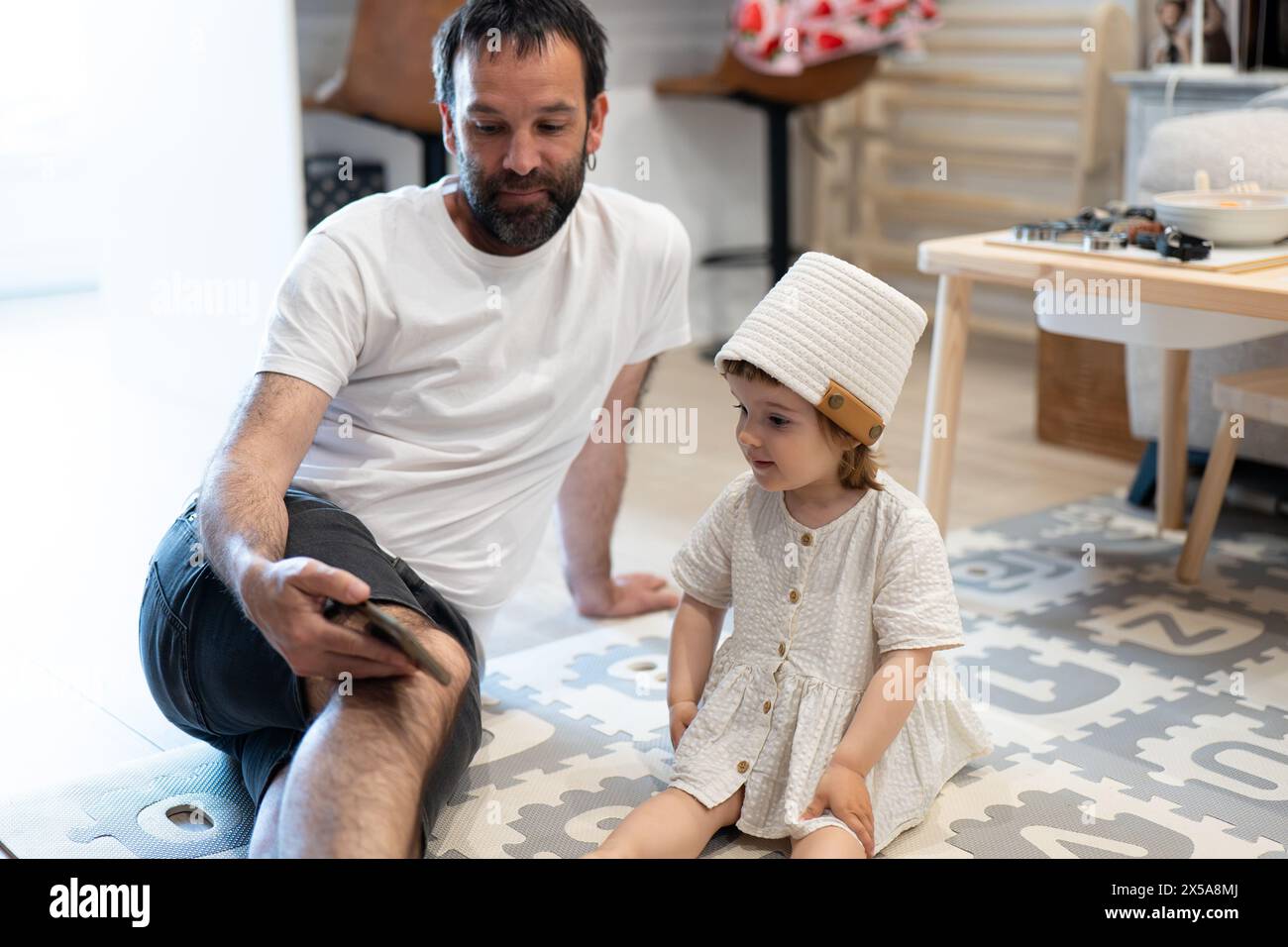 A father sits on the floor showing something to his young daughter who is attentively looking on Stock Photo