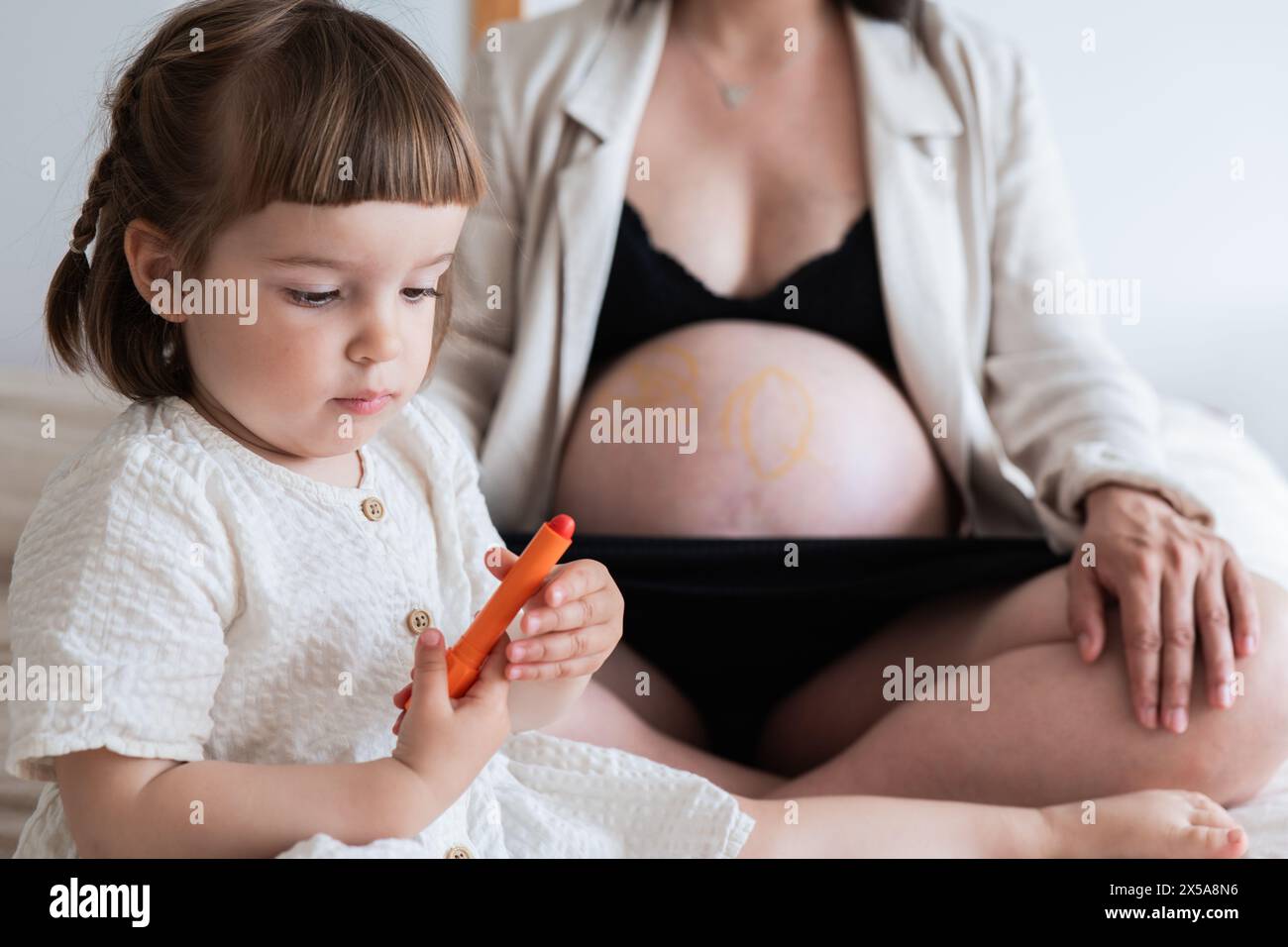 Little girl drawing a heart on her expecting mothers belly, expressing love and sibling bond Stock Photo