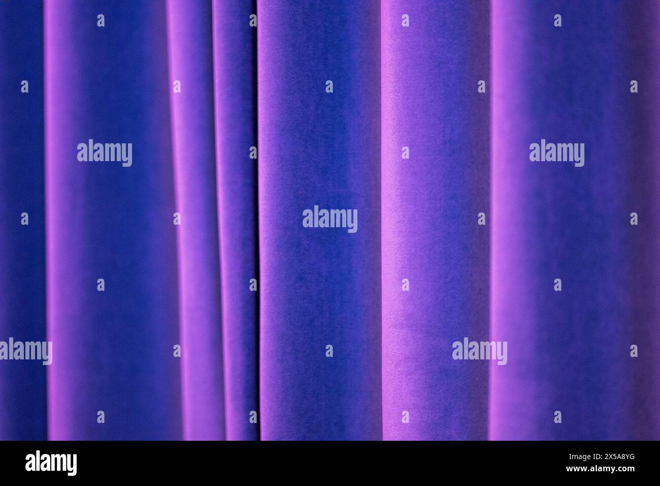 A close-up of purple curtains with a smooth texture illuminated by soft, diffused lighting creating a calming abstract pattern. Stock Photo