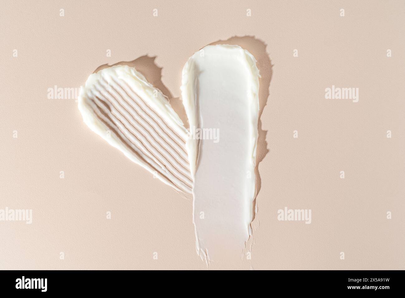 A creative display of two white cream textures forming a heart-shape against a smooth beige backdrop, perfect for skincare or culinary themes Stock Photo