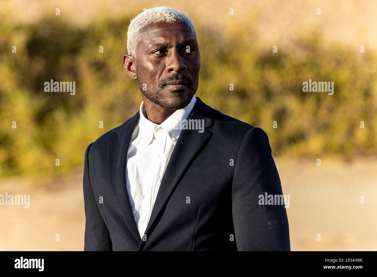 An African American male model with silver hair, dressed in a formal suit, poses on a sunny beach Stock Photo
