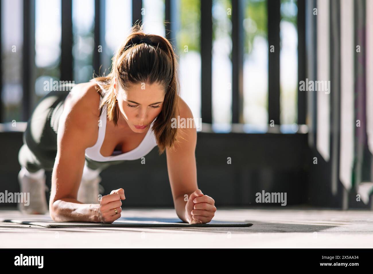 A focused athletic woman performing a plank exercise in her home environment, showcasing determination and fitness discipline Stock Photo