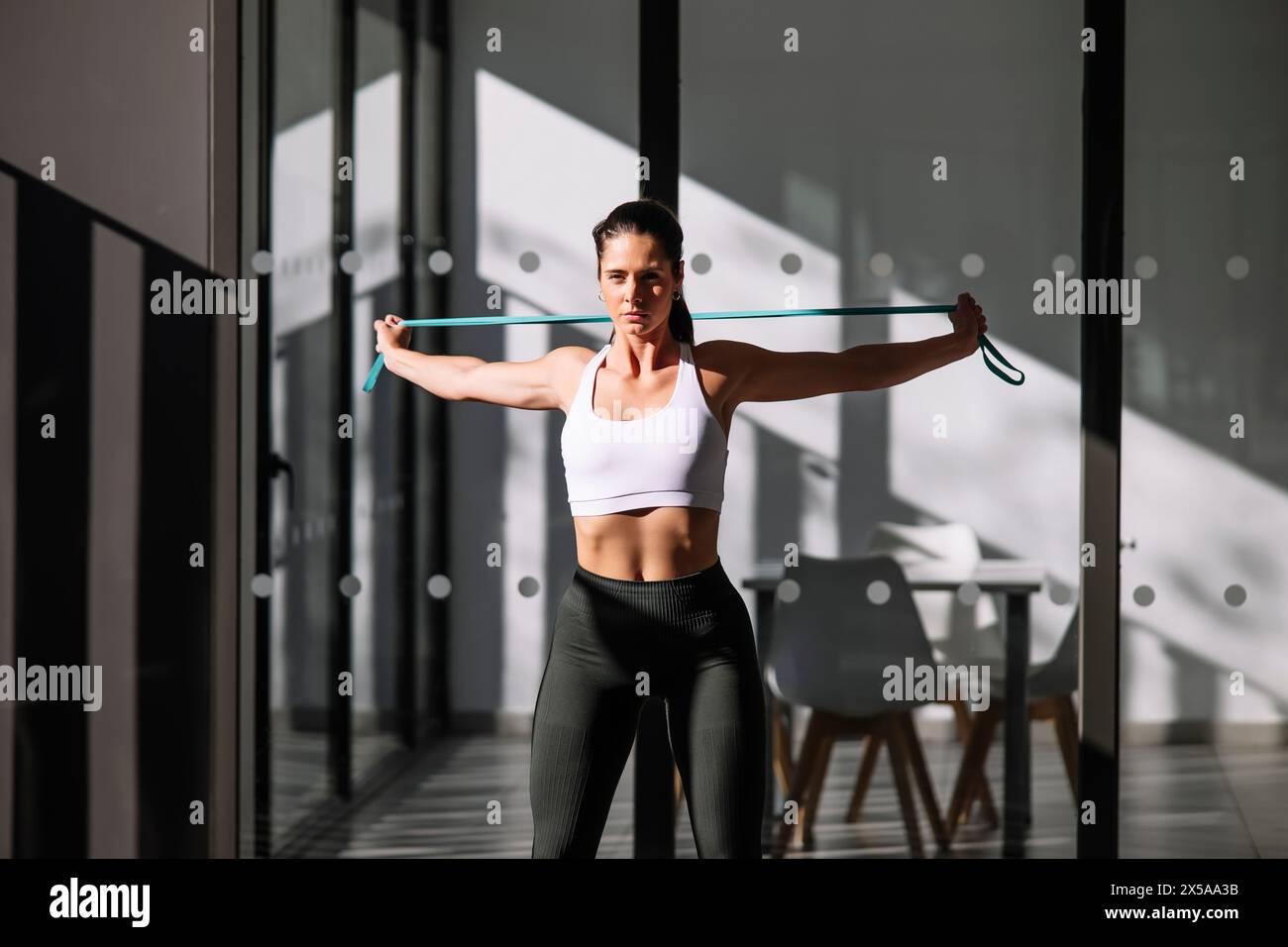 A focused female athlete uses a resistance band for a home workout in a modern, sunlit space Stock Photo