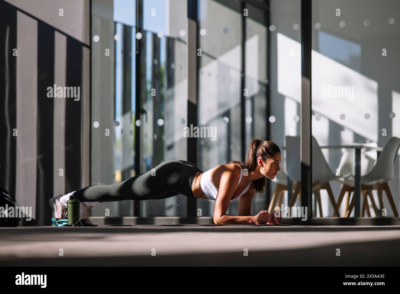 A fit young woman is doing a plank exercise in a brightly lit home environment with modern decor Stock Photo