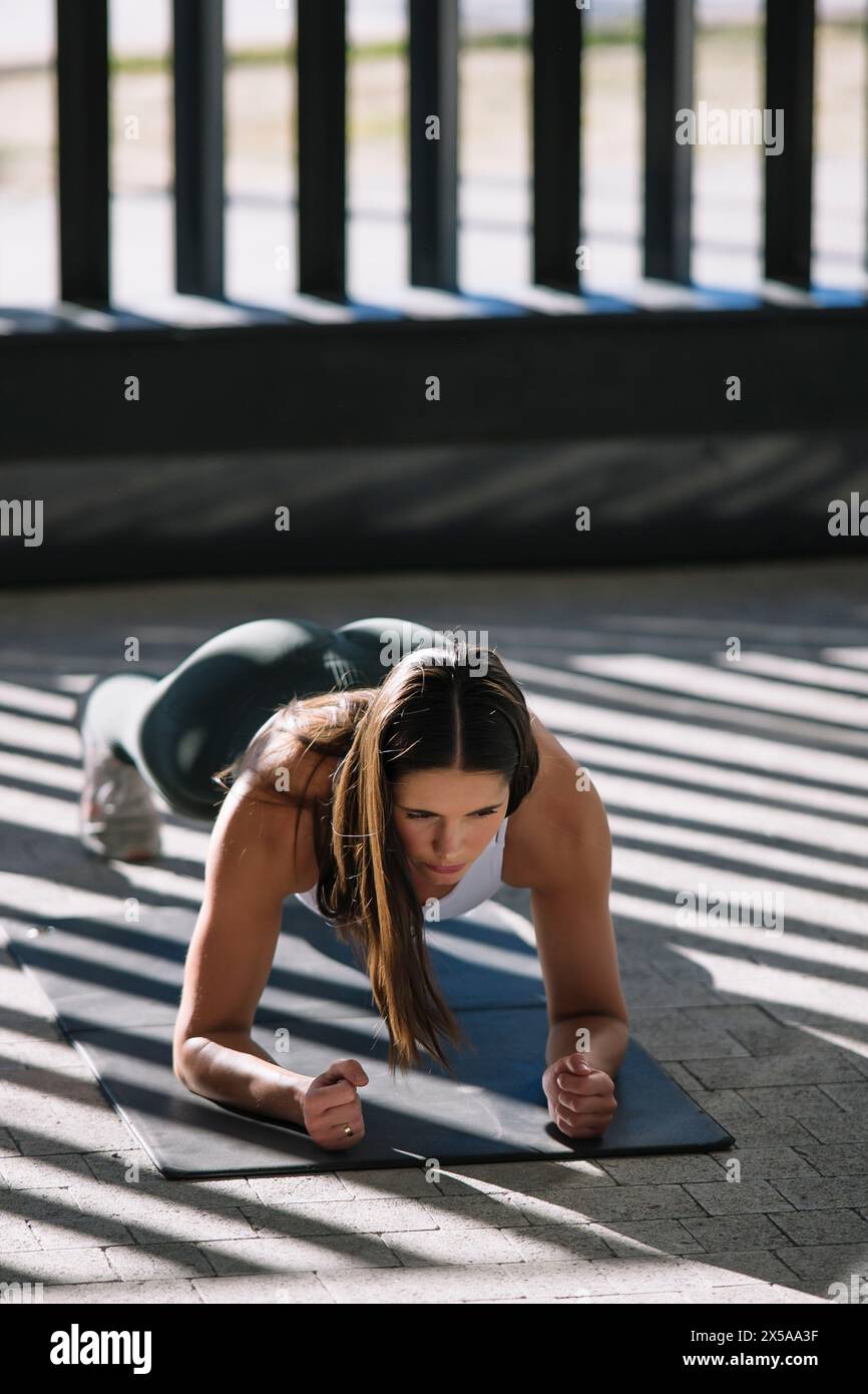 A dedicated woman engages in a plank exercise on a mat at home, showcasing her focus and commitment to fitness Stock Photo