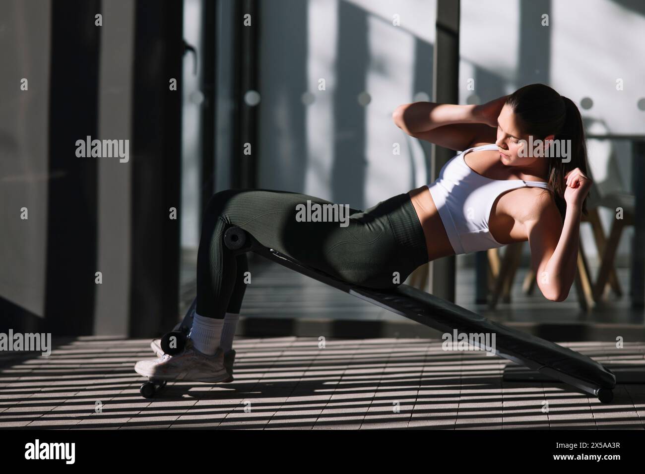A focused female athlete performs abdominal exercises at home, showcasing a healthy and active lifestyle Stock Photo