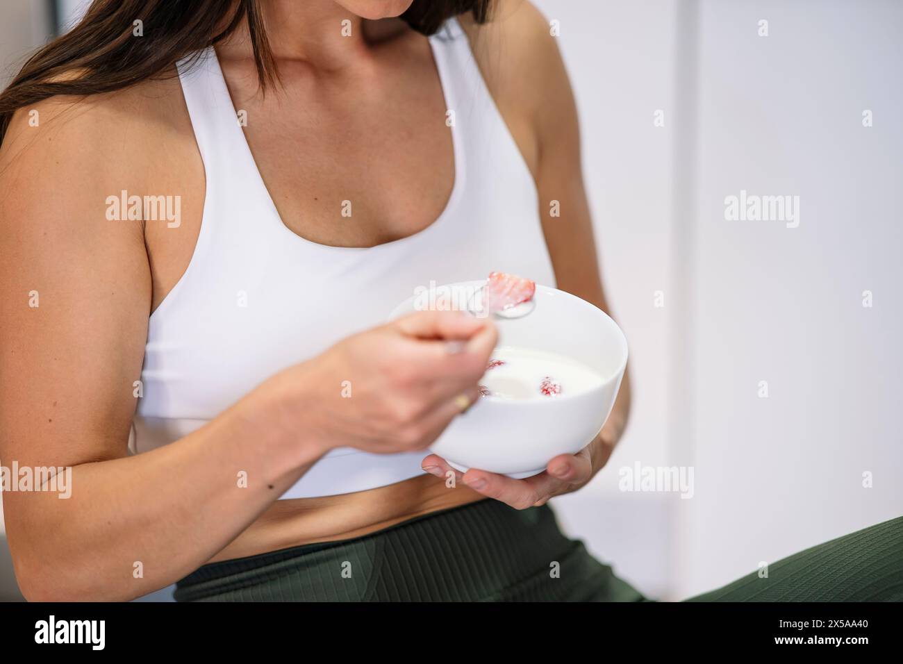 A fit woman in workout attire enjoys a healthy bowl of yogurt with fruit, emphasizing a balanced lifestyle Stock Photo