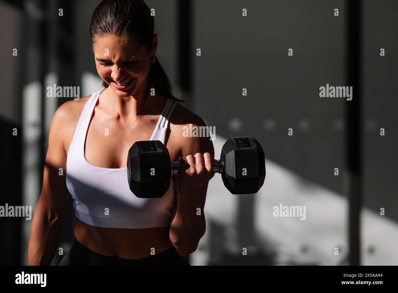 A focused athletic woman lifts weights at home, showcasing strength and dedication to fitness Stock Photo