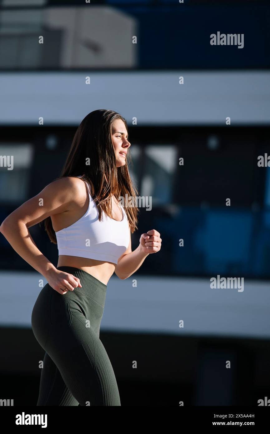 A focused female athlete in sportswear jogs near a stylish modern home, showcasing an active lifestyle Stock Photo