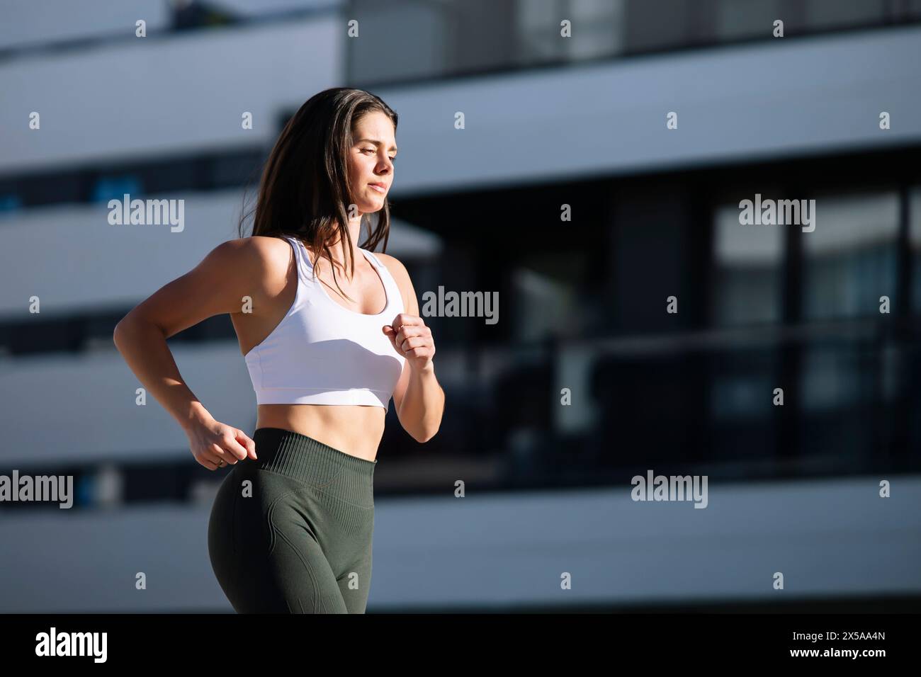 A fitness-focused woman in sportswear is jogging outside a modern building, exhibiting an active lifestyle Stock Photo