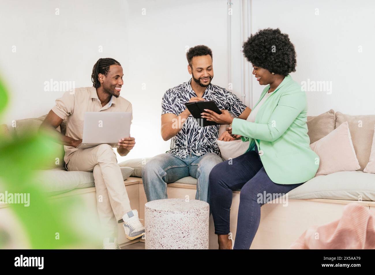 Three professionals engaging in a collaborative work session on a couch with digital devices Stock Photo