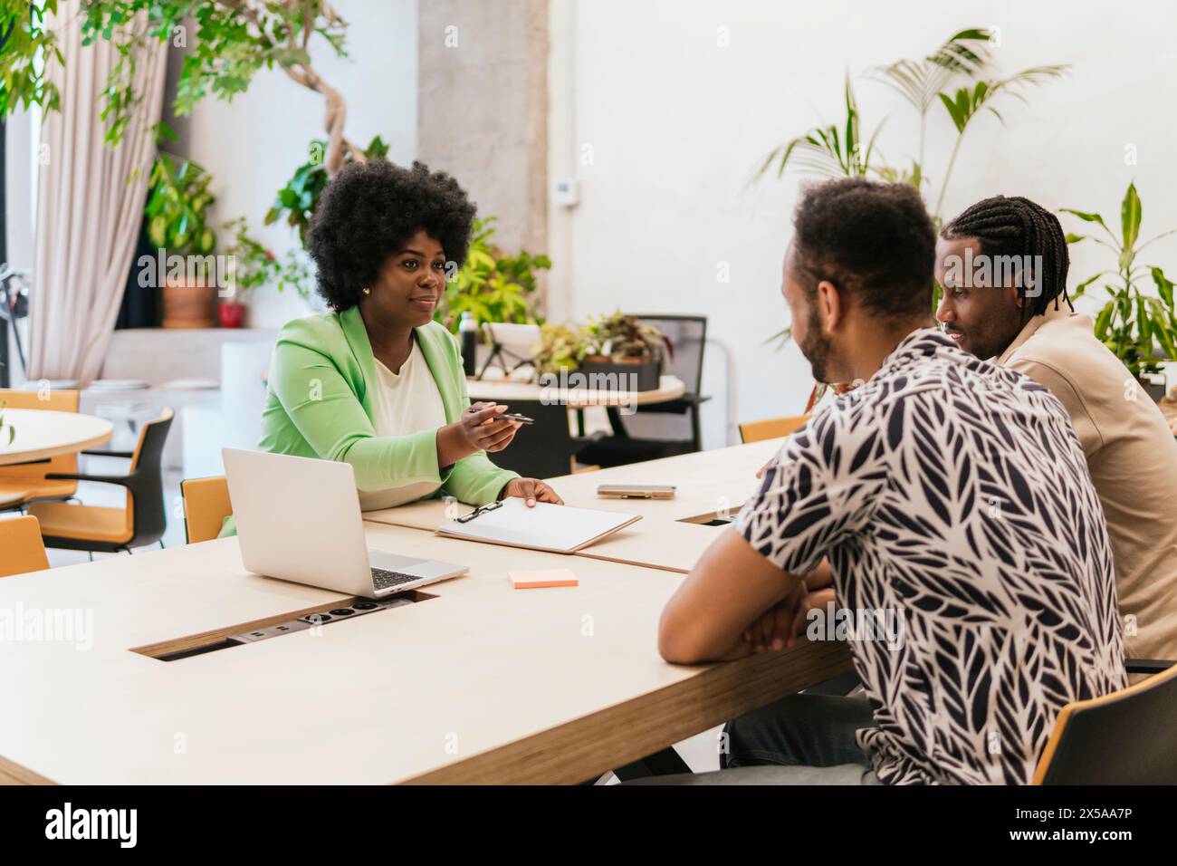 A professional, multicultural team engages in a discussion at a stylish coworking space, highlighting teamwork and creativity in a casual environment Stock Photo