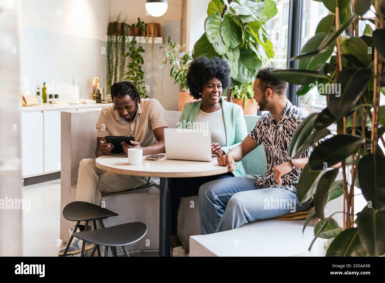Three professionals engaging in a collaborative workspace with a laptop and tablet Stock Photo