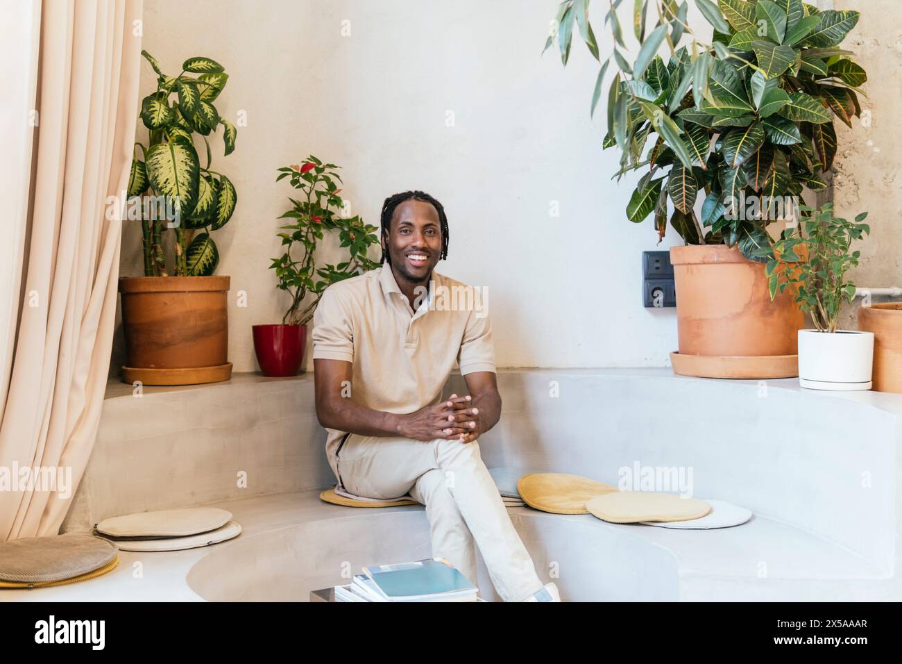 Man smiling in a modern, plant-filled coworking space, radiating a relaxed atmosphere Stock Photo
