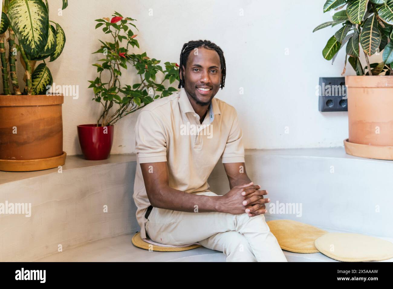 Man smiling in a modern, plant-filled coworking space, radiating a relaxed atmosphere Stock Photo