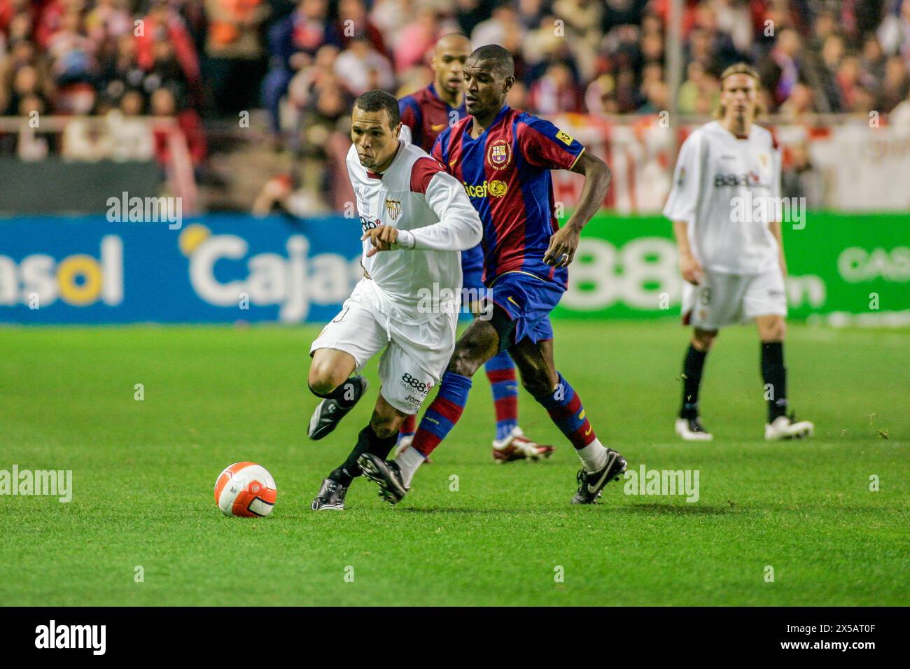 Luis Fabiano deftly maneuvers around Eric Abidal in a tense Sevilla-Barcelona match. Stock Photo