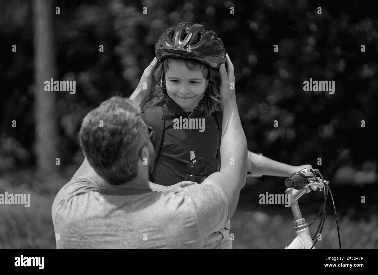 Father and son riding bike in park. Child in safety helmet with father riding bike in summer day. Father teaching son riding bike. Fatherhood. Father Stock Photo