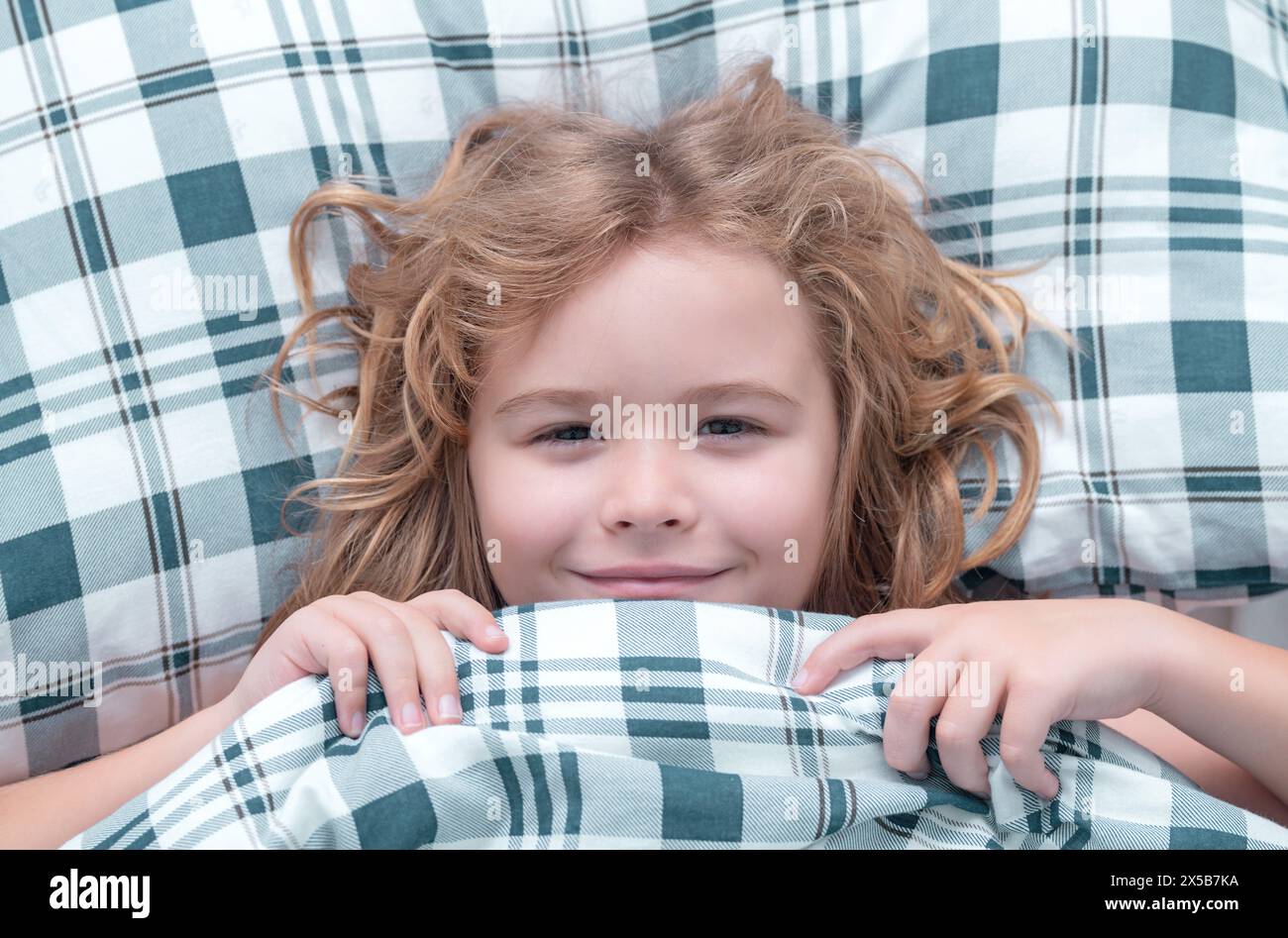 Kid under covers, face cover with blanket. Portrait of little child