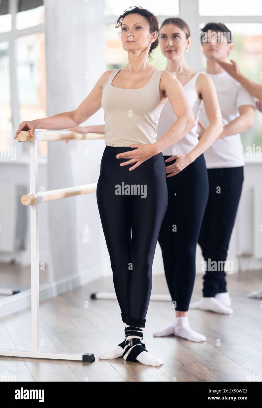 Female ballet teacher exhibiting third position at barre during group ...