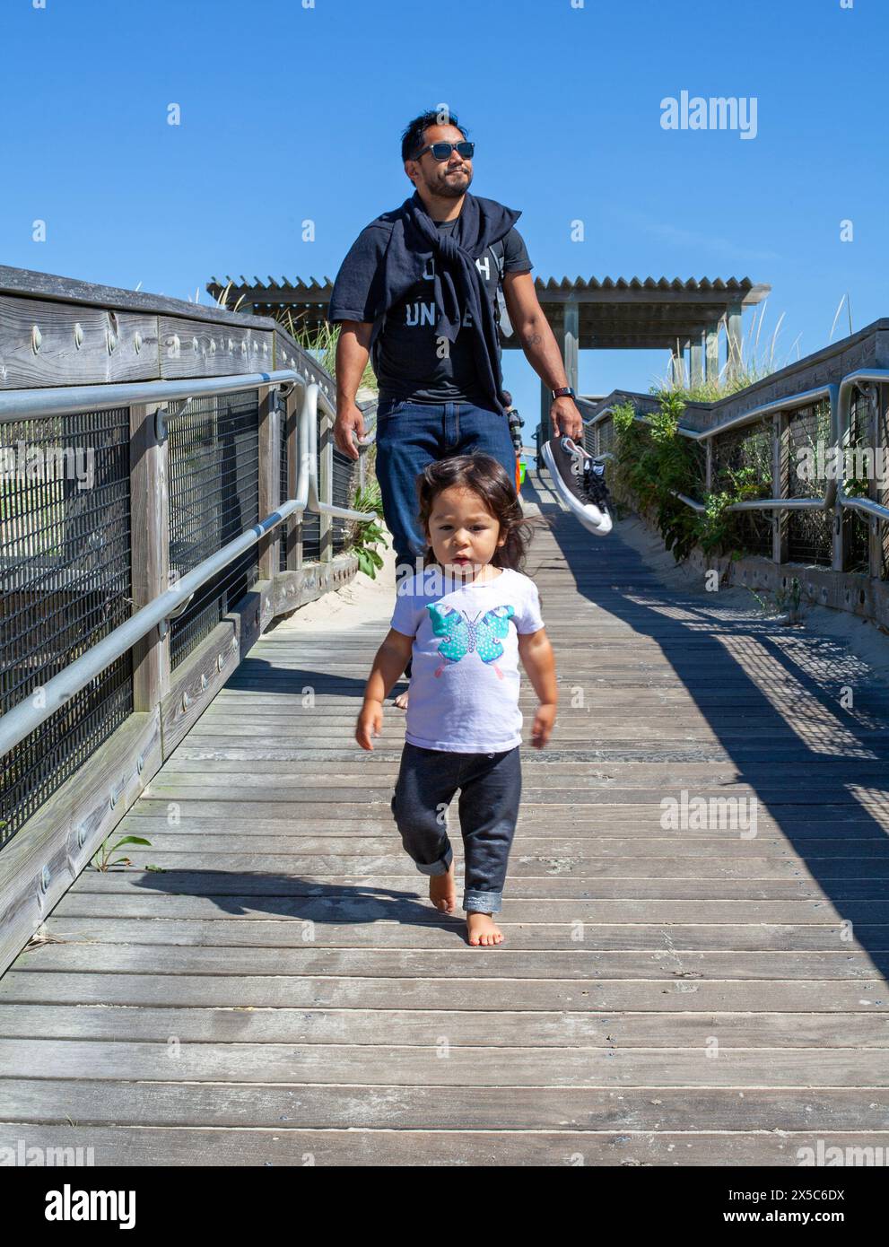 A father and his daughter walk on a boardwalk towards the ocean in Massachusetts, USA. Stock Photo