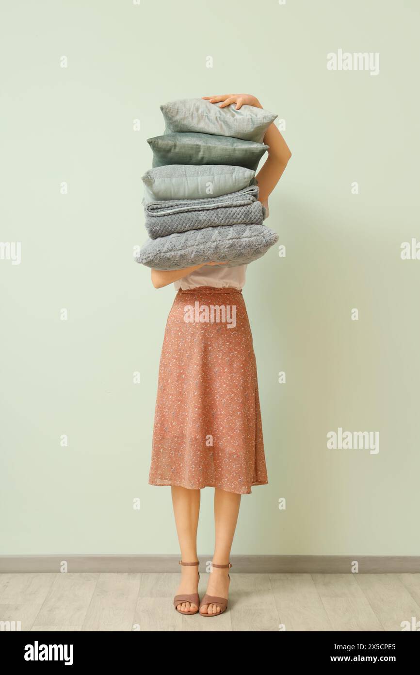 Woman with stack of pillows and folded warm plaid near light wall Stock Photo