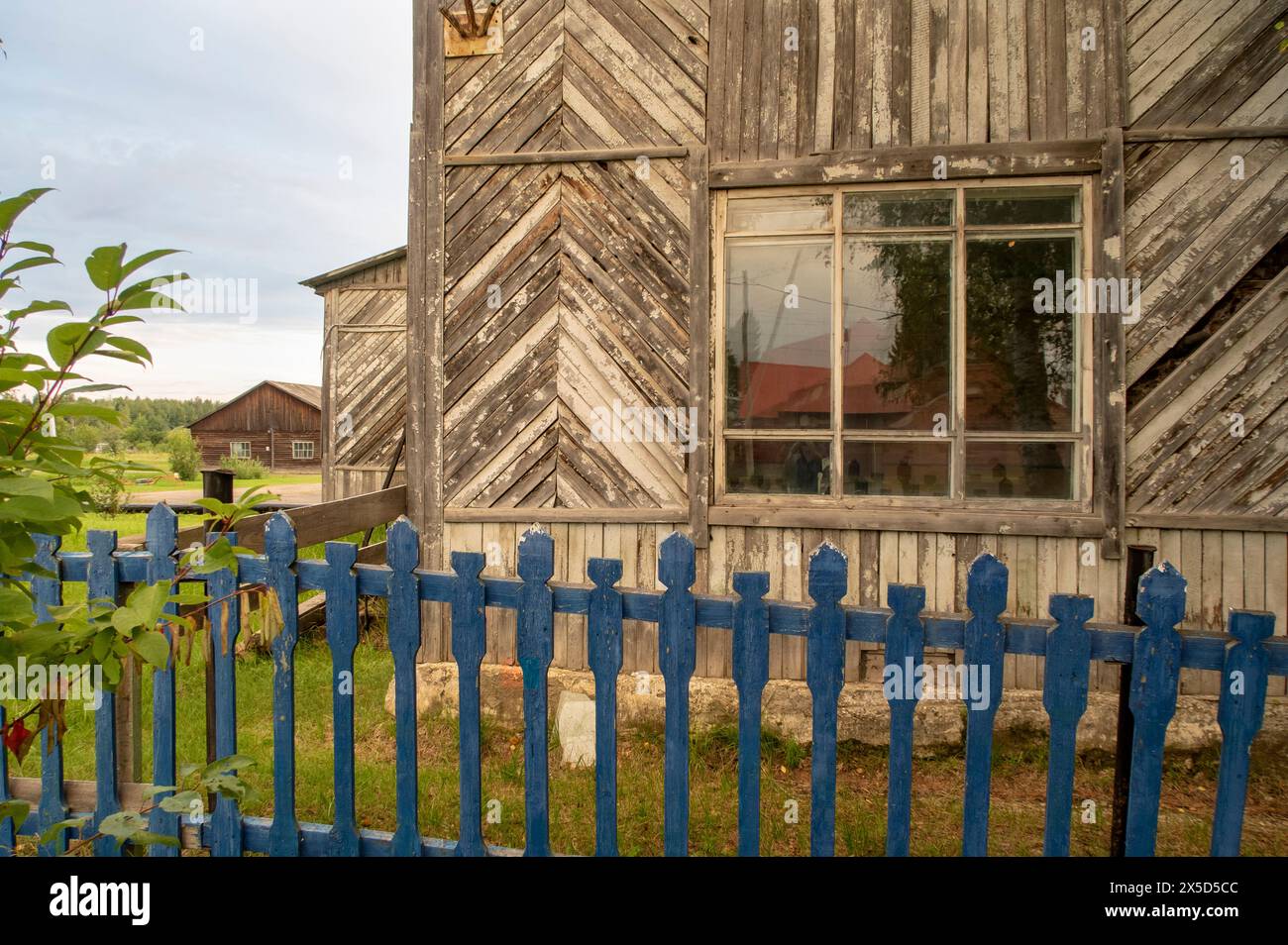 A fragment of a wooden house with an old blue fence in the village in the evening Stock Photo