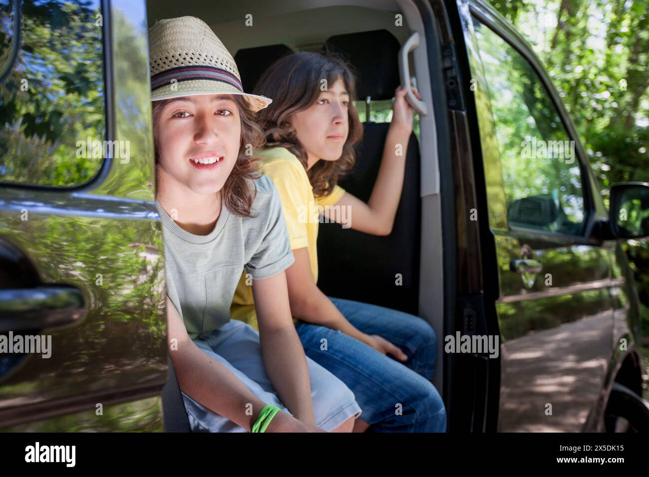 Two twin brothers are sitting in a van, one wearing a yellow shirt. They are smiling and seem to be enjoying their time together Stock Photo