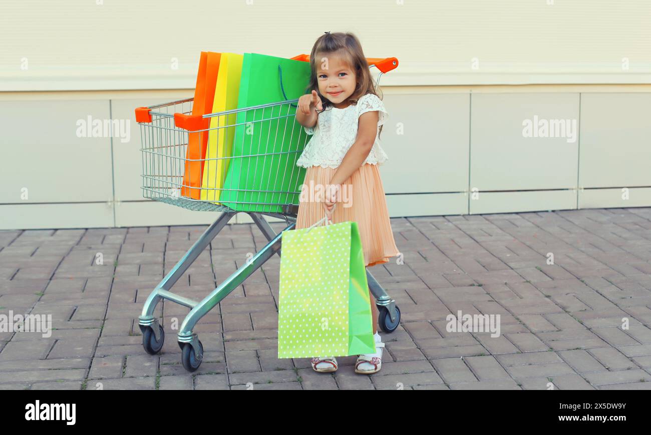 Happy little girl child with trolley cart and colorful shopping bags ...