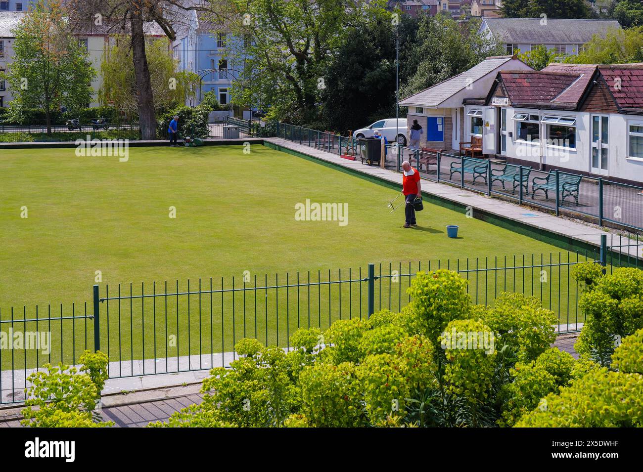 Maintenance of the bowling lawn at Dawlish Bowling Club in Devon by two groundsmen. One mowing and one seeding. Stock Photo