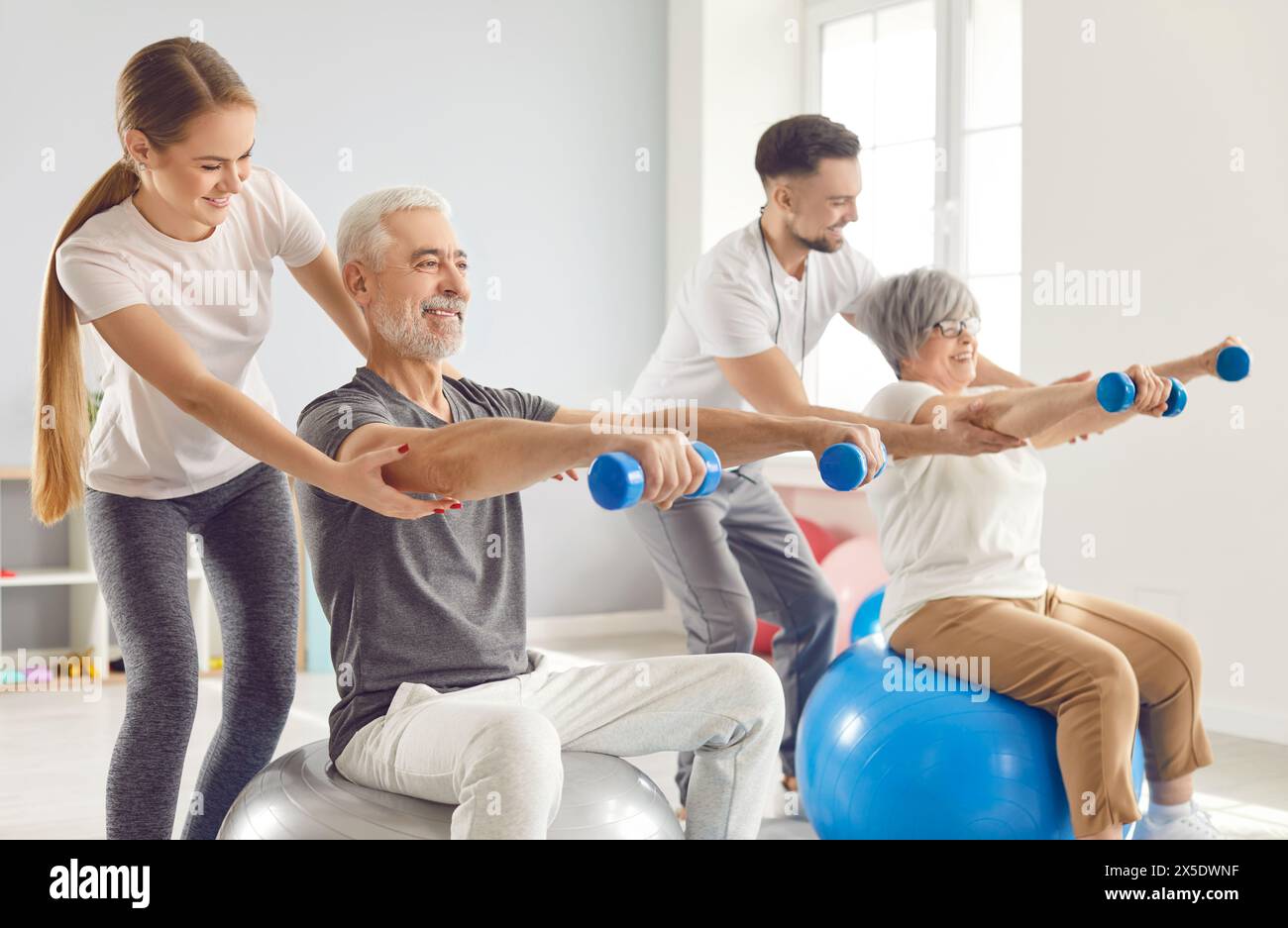 Coach or health care worker helping mature people to do sport exercises with dumbbells Stock Photo
