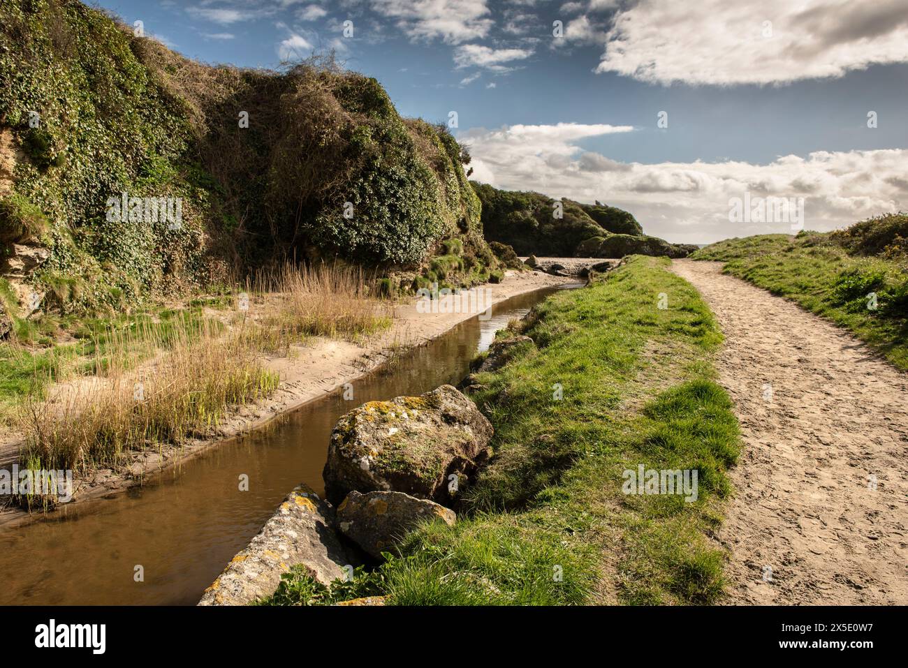 A rough sandy footpath next to the Par Polmear River flowing towards the sea at Par Beach in Cornwall in the UK. Stock Photo