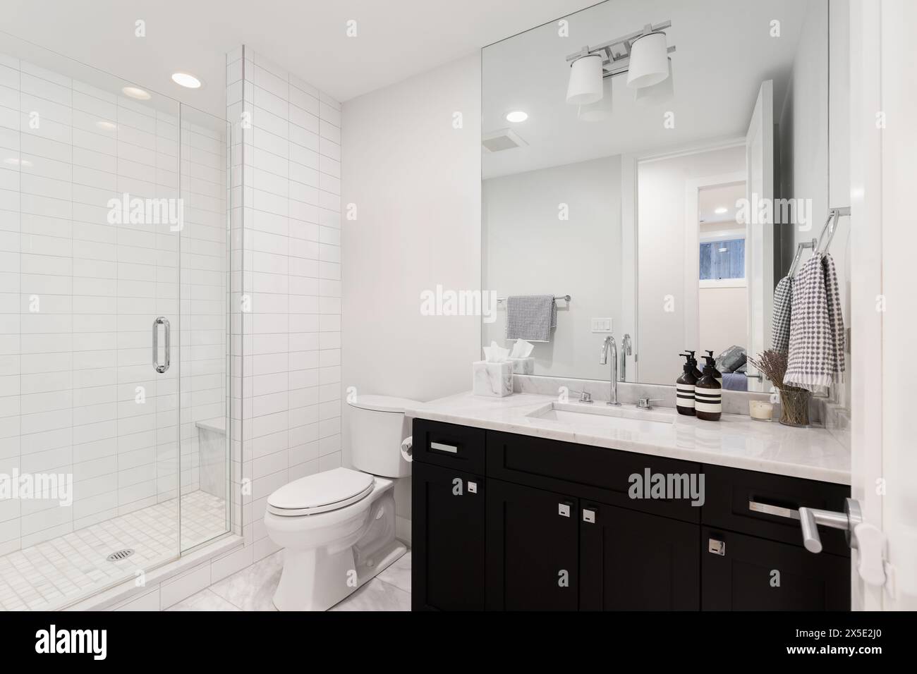A bathroom with a black cabinet, white marble countertops, and a walk ...