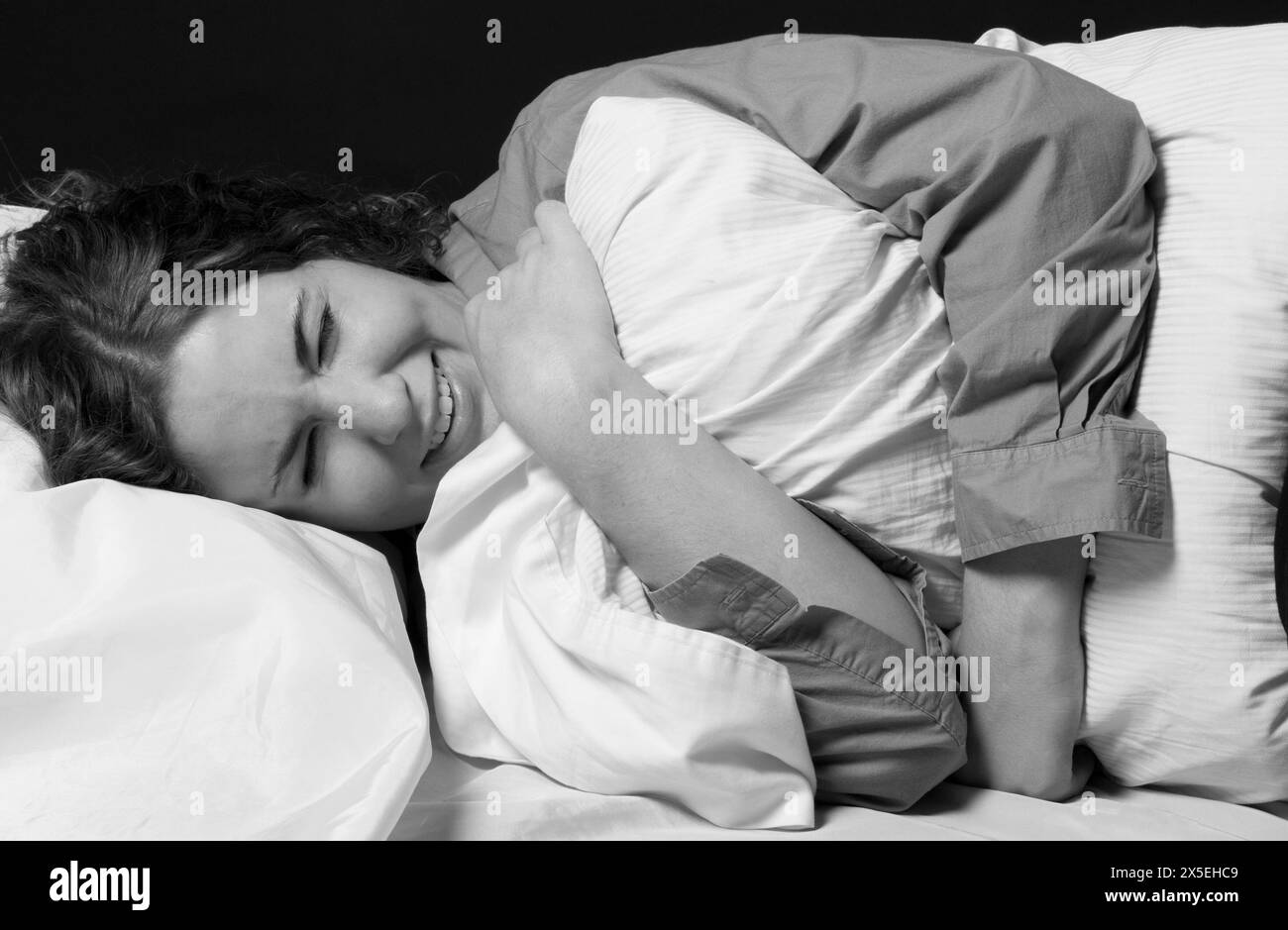 Young woman holding a pillow to her stomach, experiencing stomachache or cramps.Concept of stomachache or stomach cramps. USA Stock Photo