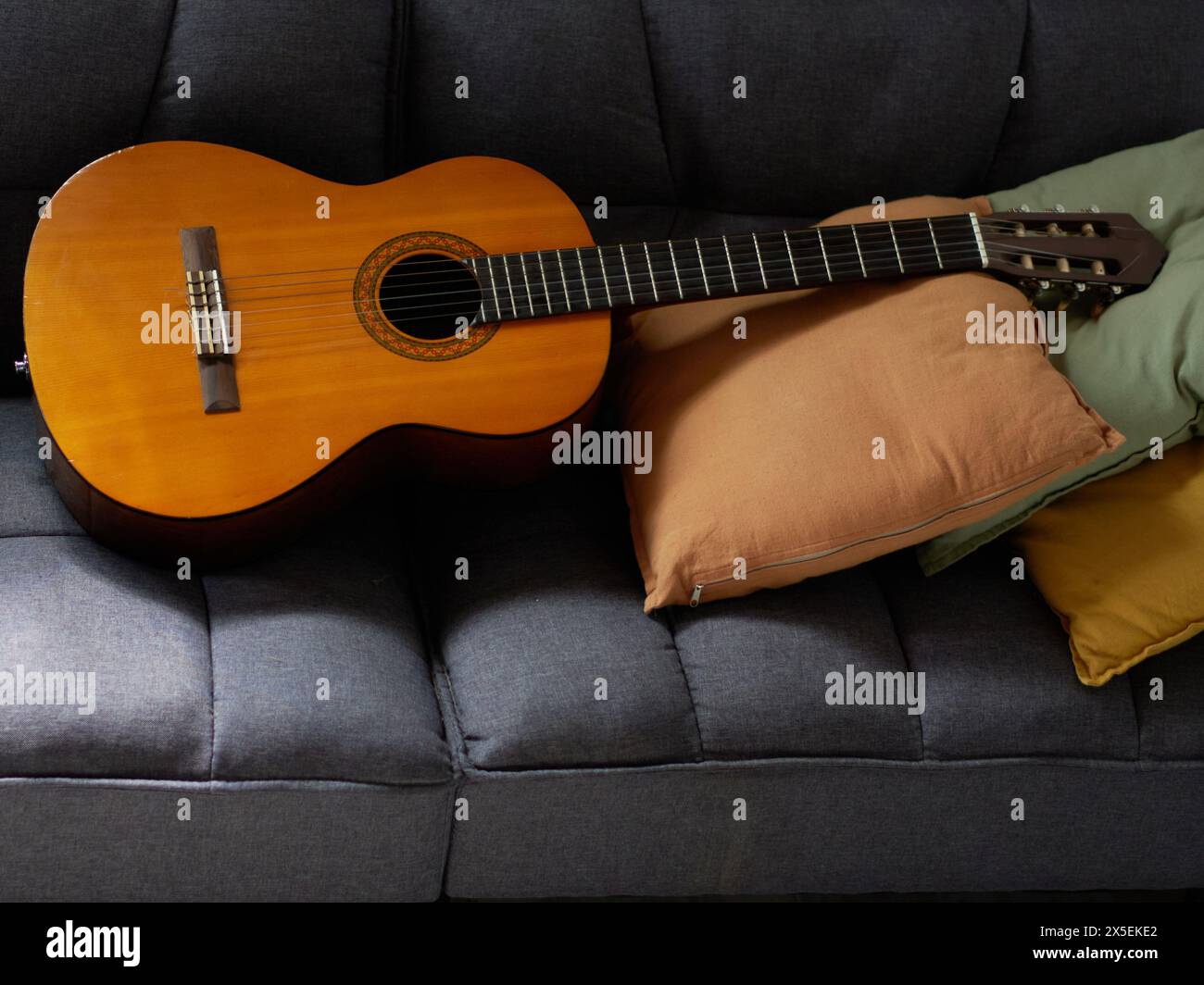 classical guitar lying on top of a gray armchair with decorative pillows. Stock Photo