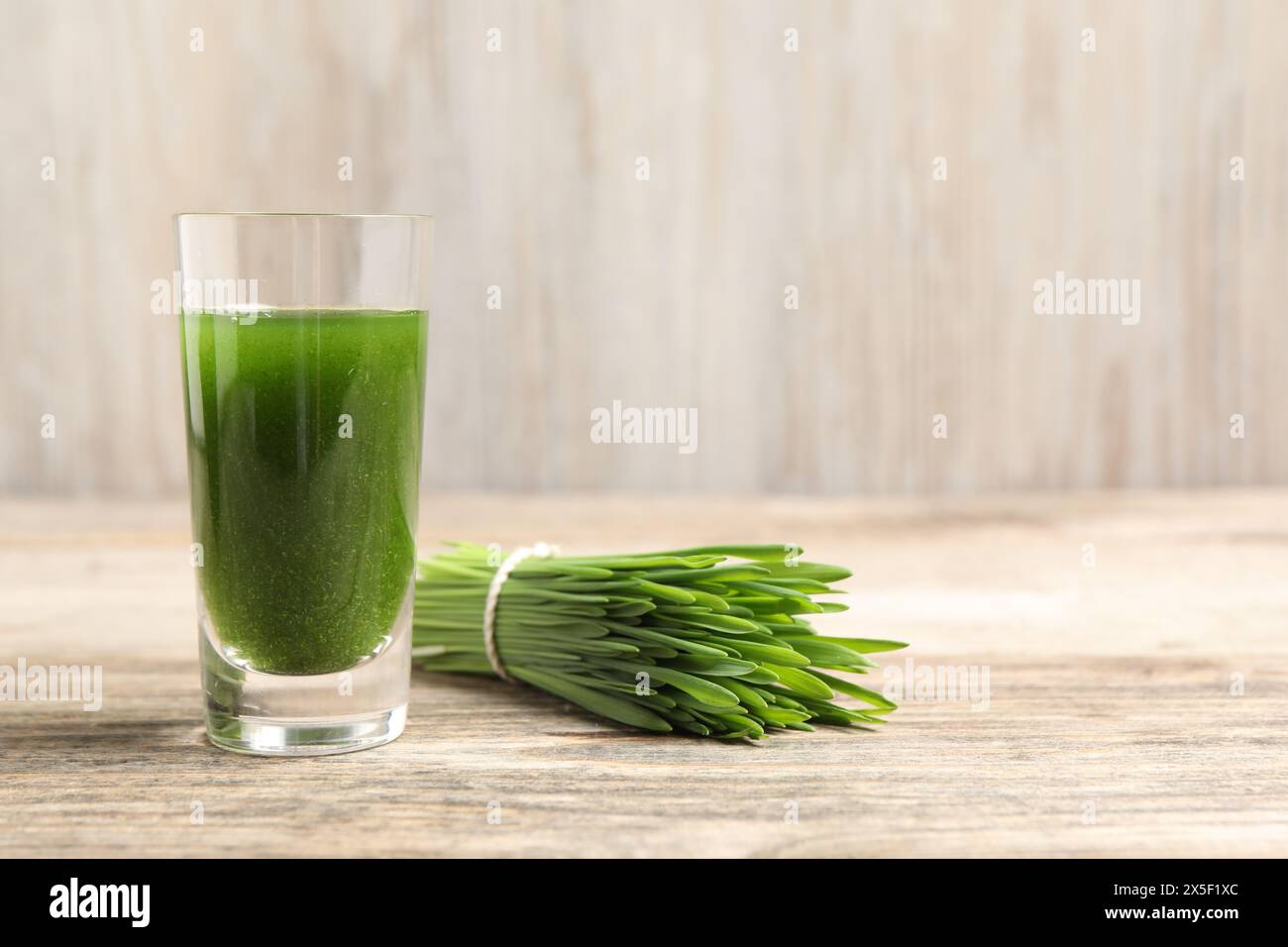 Wheat grass drink in shot glass and fresh green sprouts on wooden table, closeup. Space for text Stock Photo
