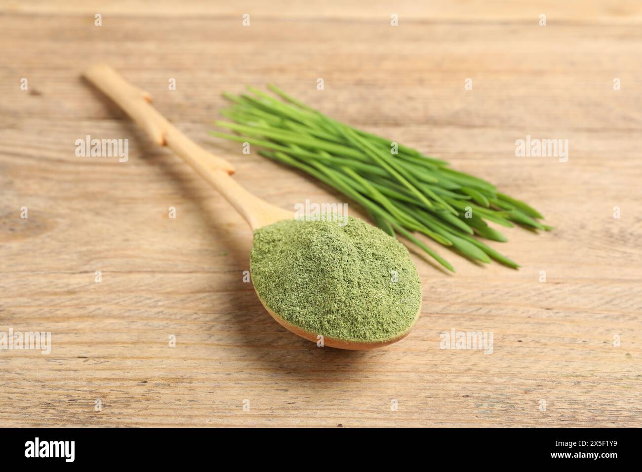 Wheat grass powder in spoon and fresh green sprouts on wooden table, closeup Stock Photo
