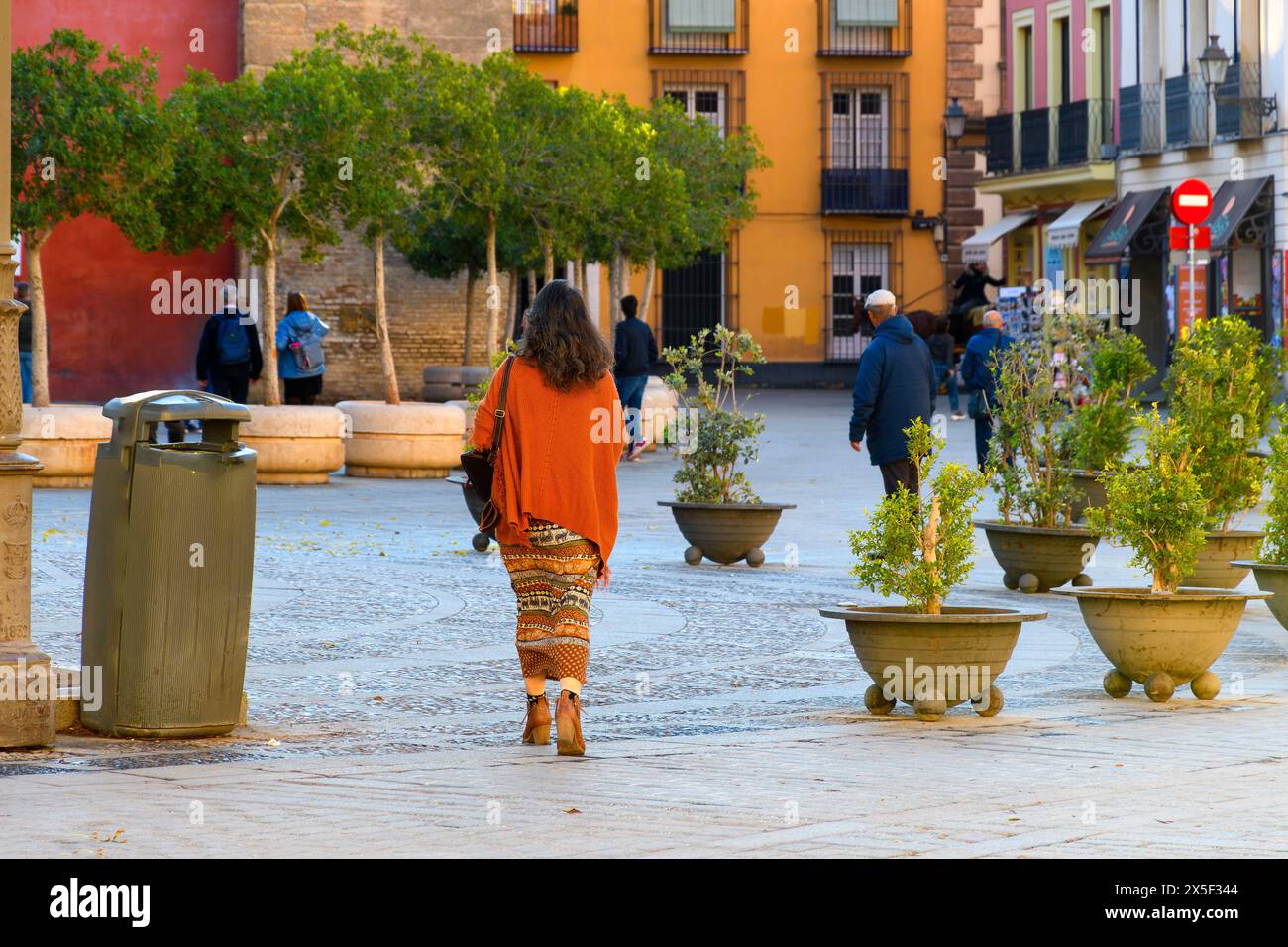 A Spanish woman dressed in traditional colors walks through Plaza Virgen de los Reyes in the Barrio Santa Cruz district of Andlusian Seville Spain. Stock Photo