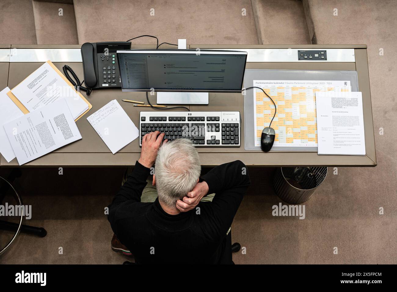 Brussels, Flemish Parliament, May 8, 2024 - Official at work, organising the debate using a PC, paper notes and the parlementary calendar as a guide Stock Photo
