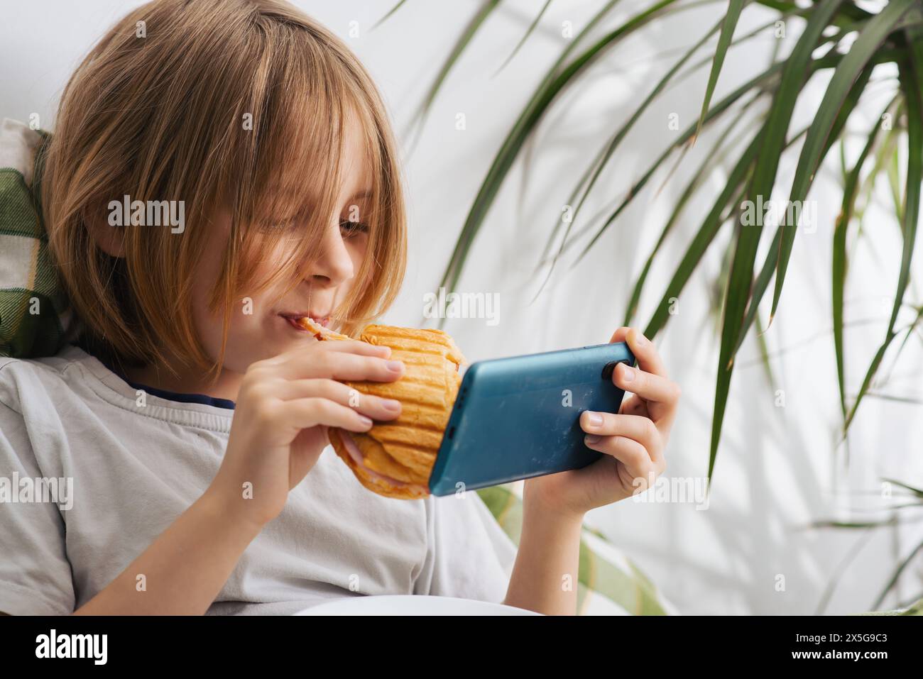 In the bed, a 9-10-year-old boy with lengthy hair savors a toast ...