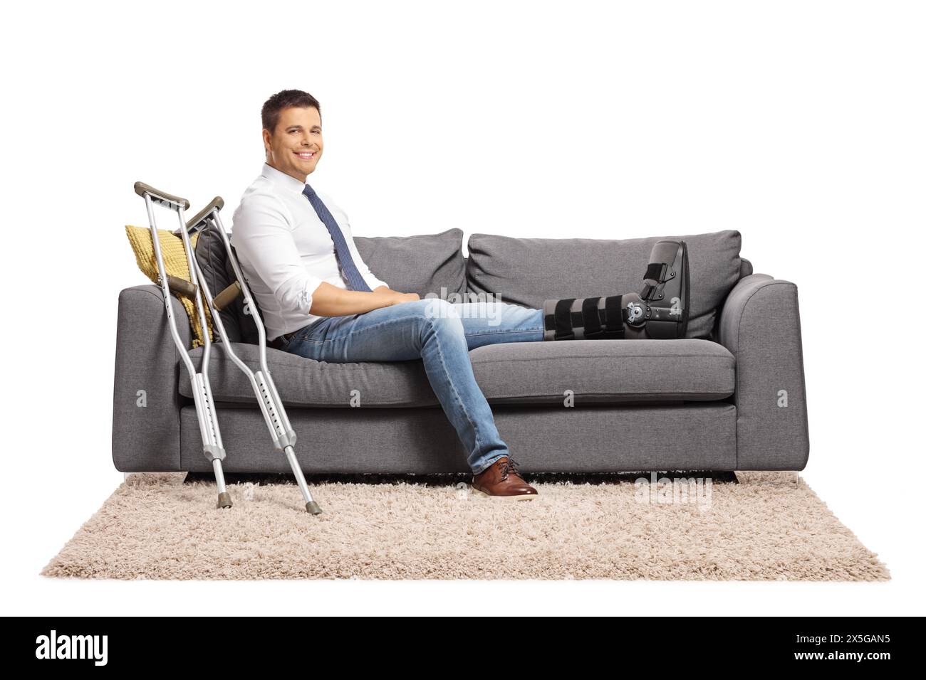 Businessman with a foot injury and leg brace sitting on a sofa isolated on white background Stock Photo