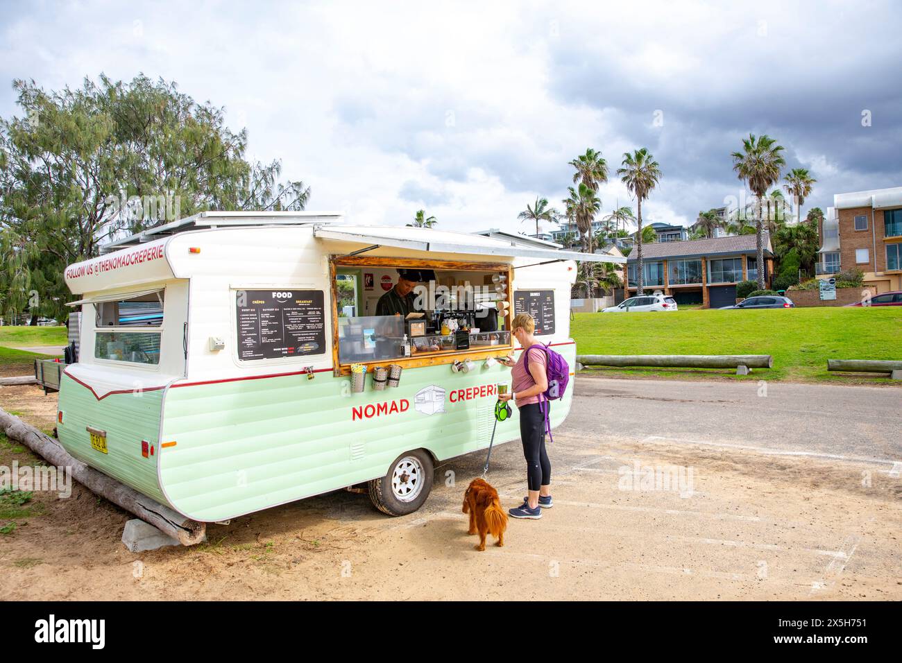 Mobile food and drink creperie stall in vintage caravan parked in Curl Curl, model released woman with pet cavoodle orders food,Sydney,NSW,Australia Stock Photo