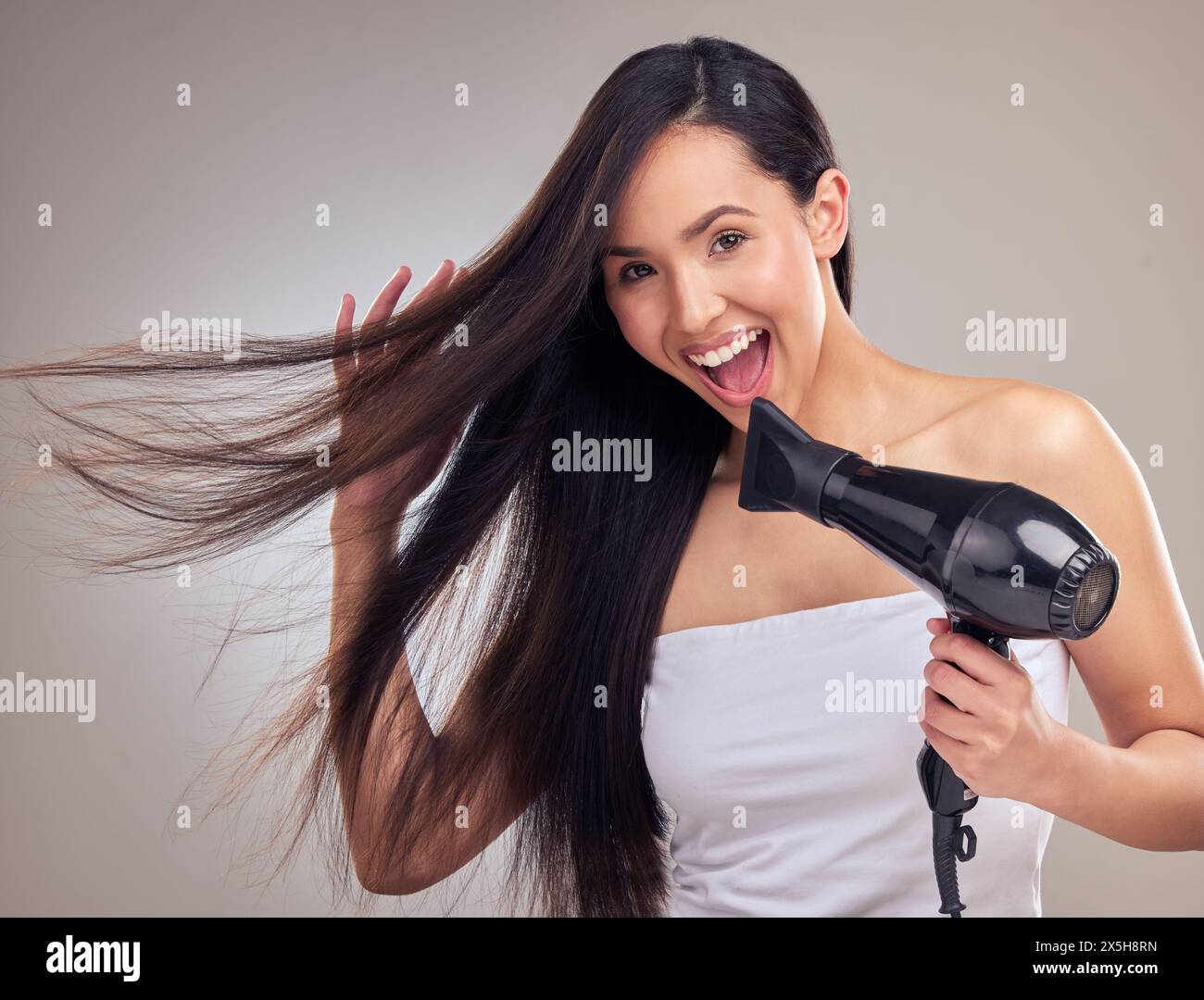 Asian woman hairdryer and happy with portrait in studio for growth straighten and brazilian treatment on gray background. Female person excited and Stock Photo Alamy