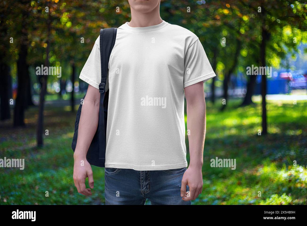 Mockup of a white men's T-shirt with a round neck, shirt on a guy with a backpack, front view, against the backdrop of a park, square. Template for fa Stock Photo