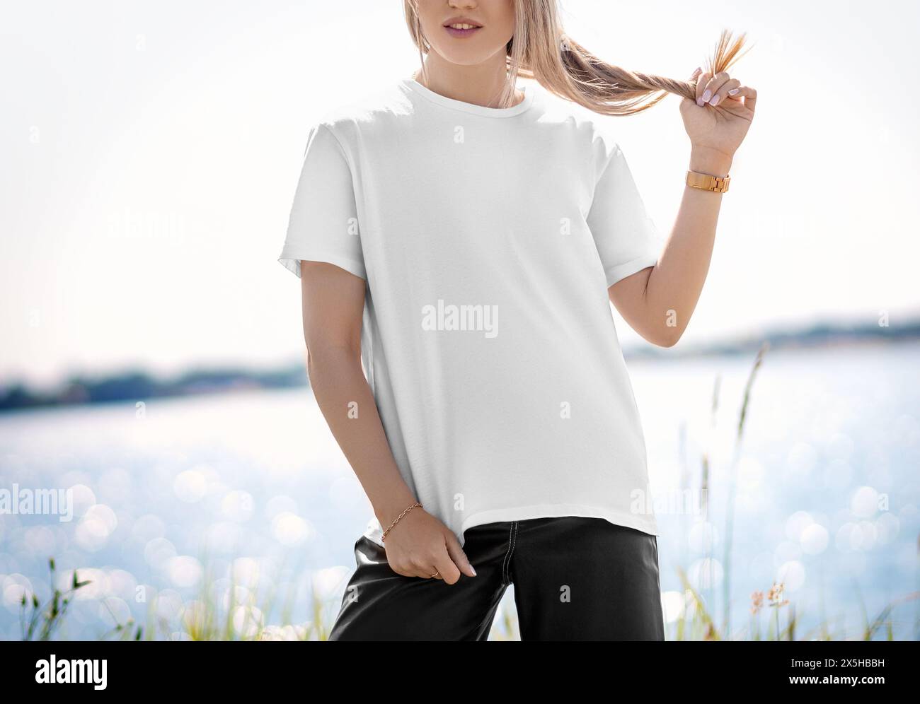 Template of a stylish white T-shirt with a round neck on a blonde girl, posing against the background of a river, front view. Female shirt mockup. Sum Stock Photo