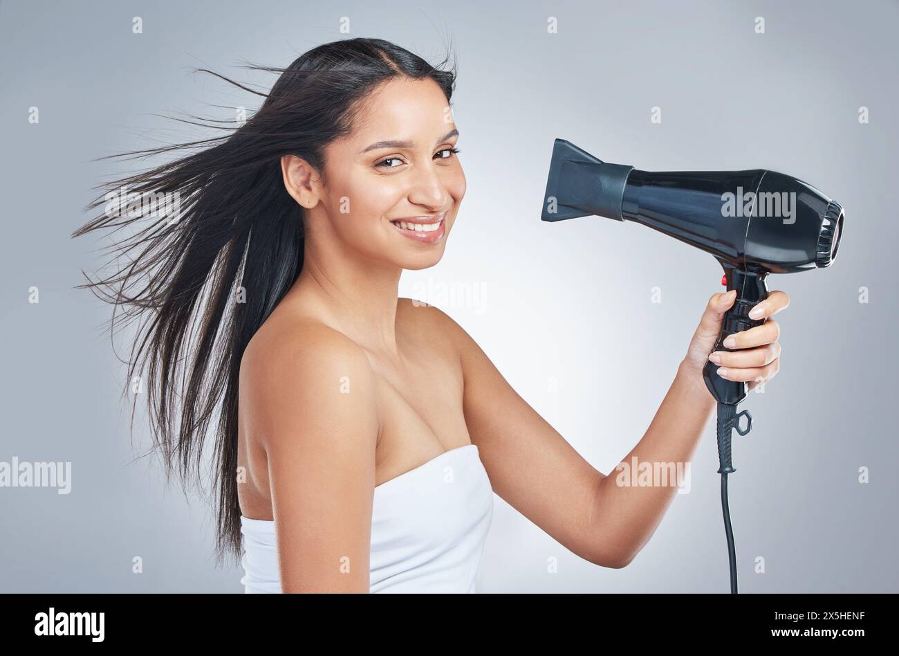 Hair, portrait and woman with hairdryer in studio for cosmetic, shine or heat protectant promo on grey background. Haircare, beauty or face of girl Stock Photo