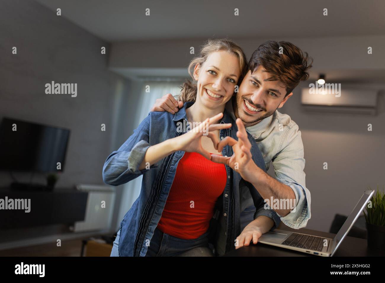 A joyful young couple forms a heart shape with their hands, smiling ...